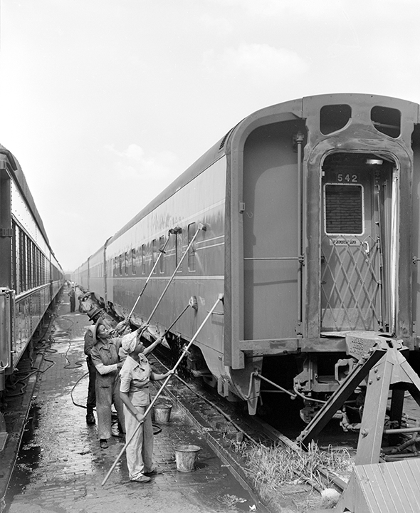 A row of women wash the side of a railroad car