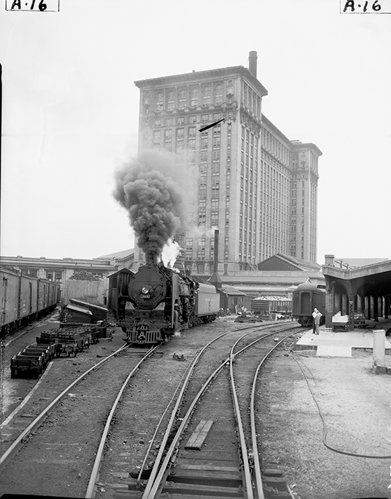 A train rolls along a track with Michigan Central Station in the background