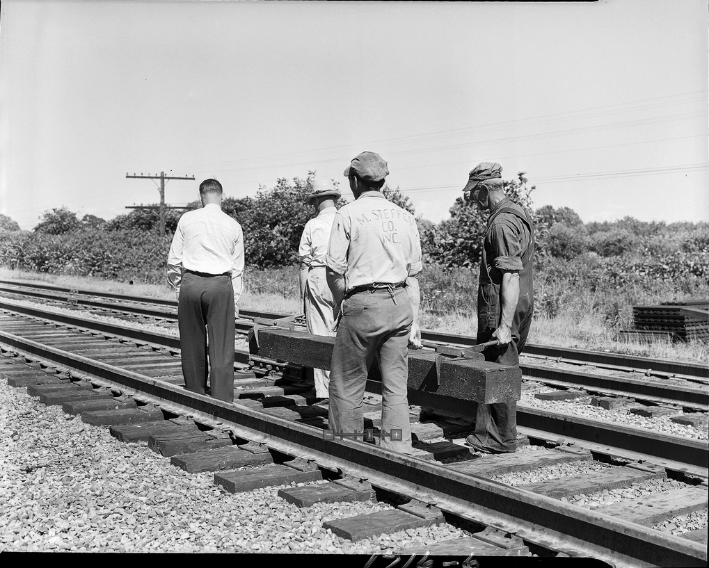 Four men carrying a railroad tie down a track