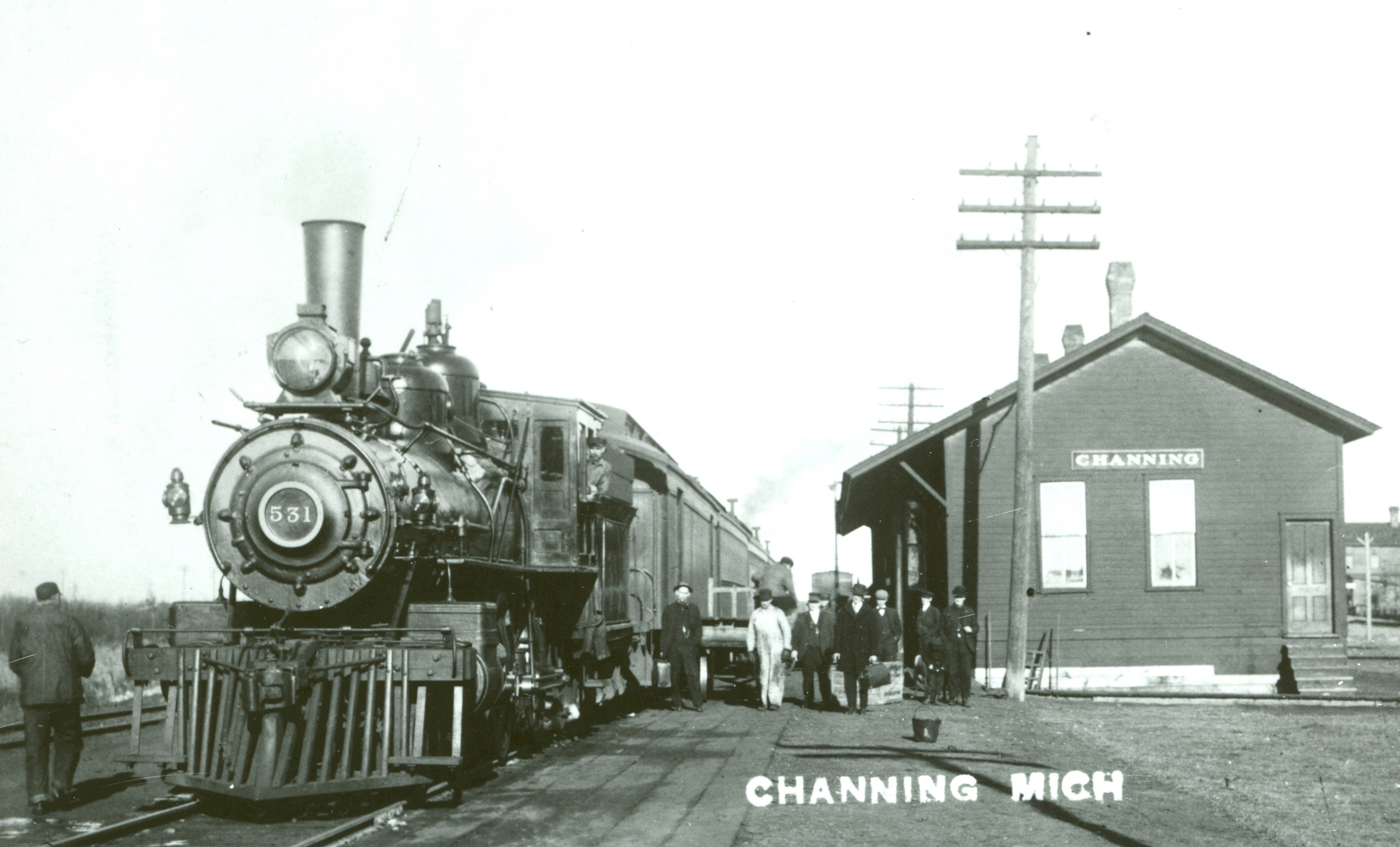 Passengers stand on a train platform between Engine 531 and the depot.