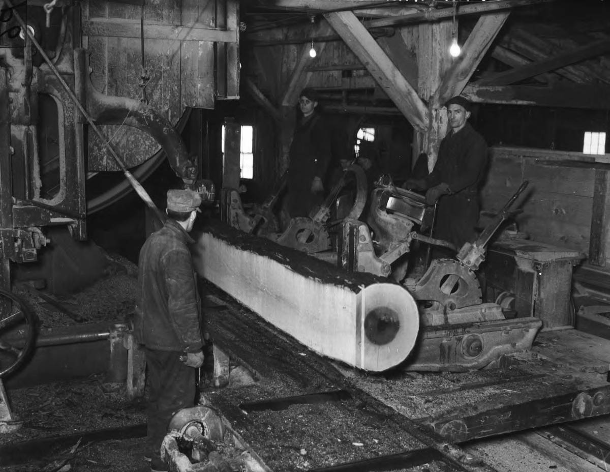 Three men stand in a sawmill sawing a large log