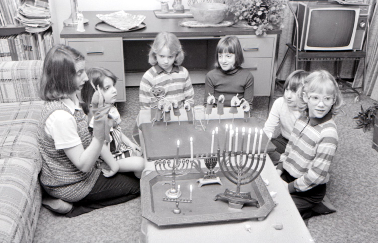 Children in a living room around a table with two menorahs