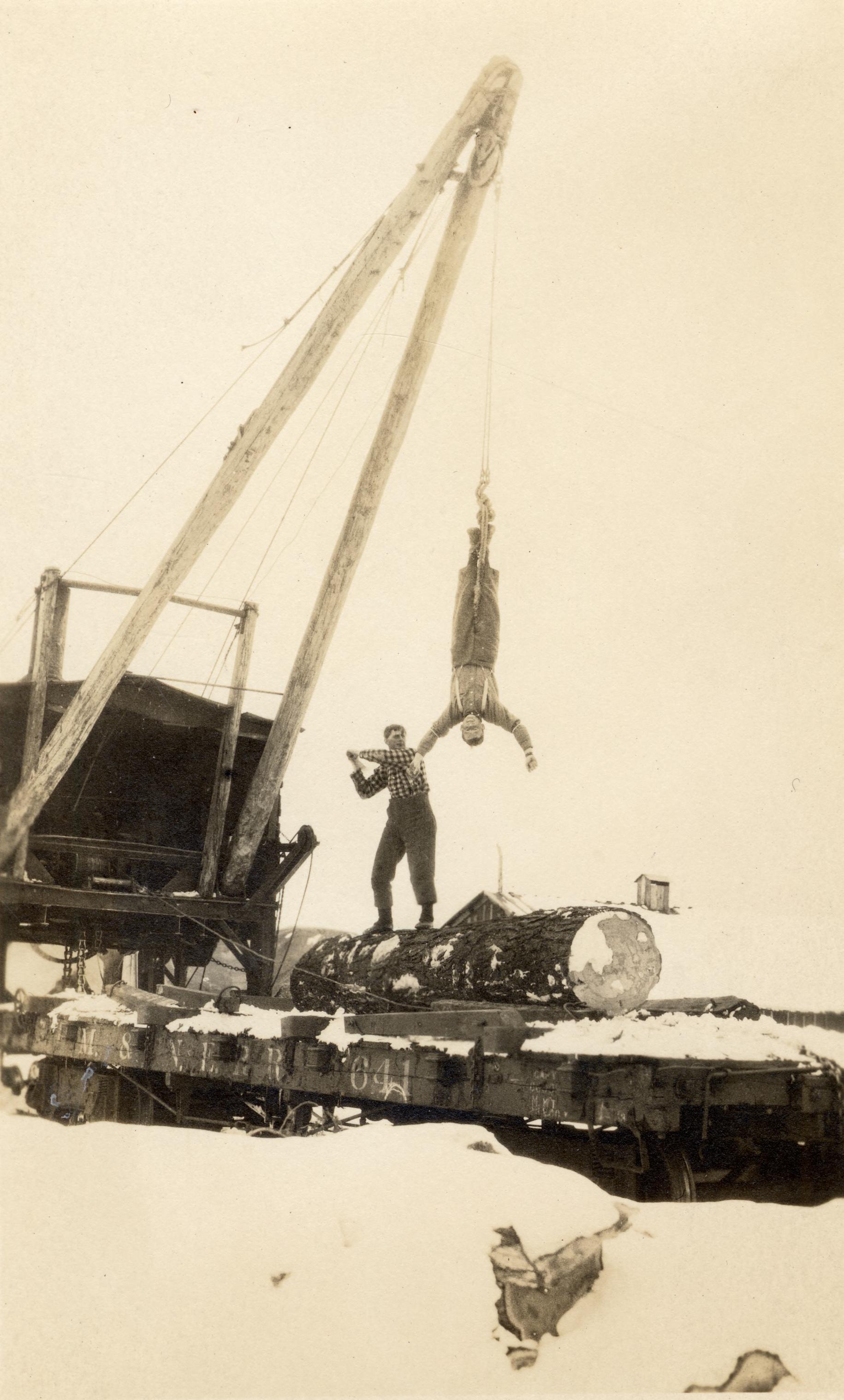 A man hangs upside down from a lumber crane