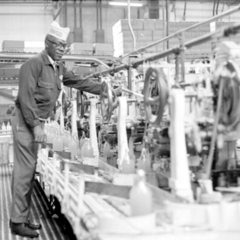 A man working in a Faygo bottling plant stands in front of the production line and makes an adjustment to the machinery.